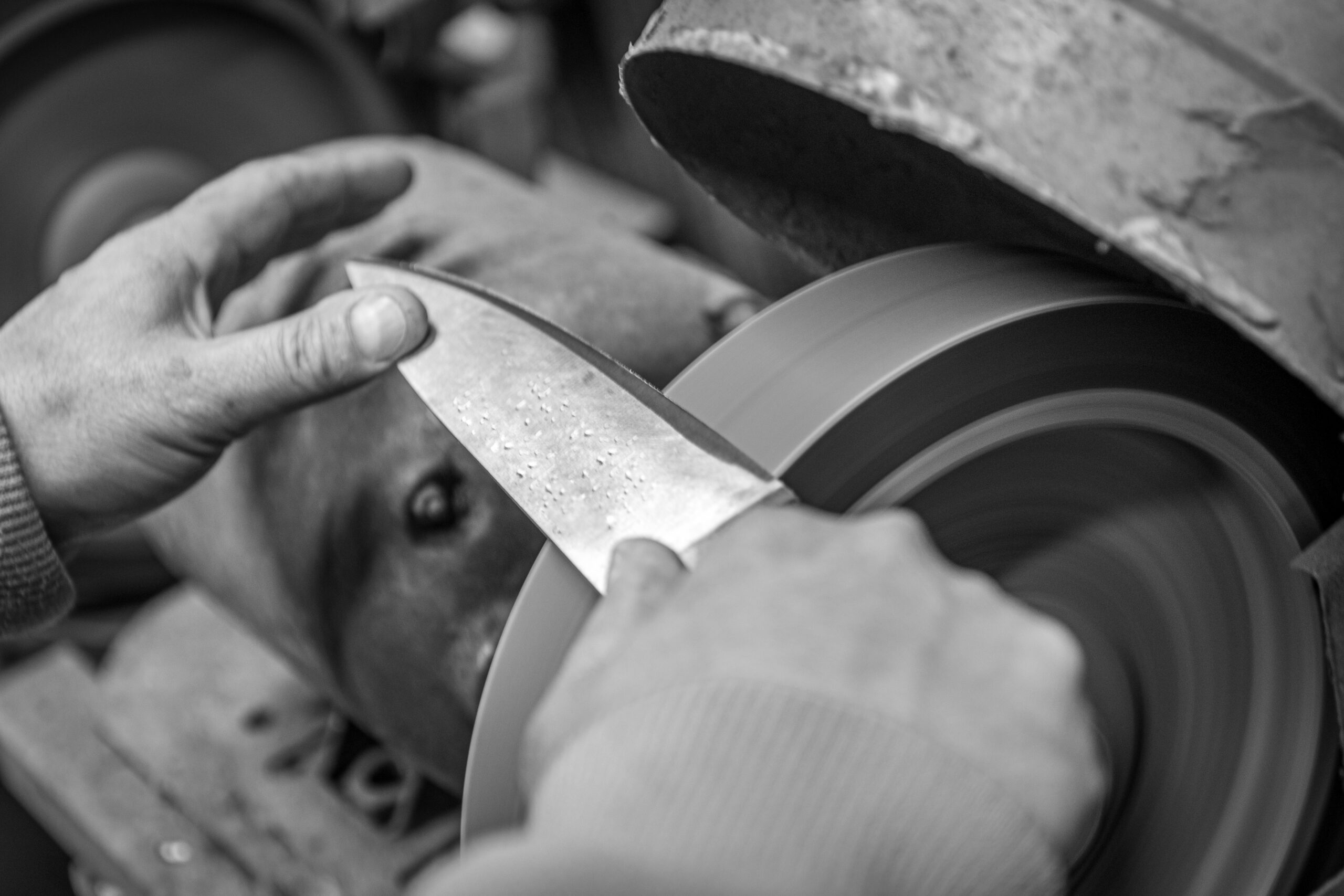 Isolated close up of chef knife sharpening, honing and stropping process by a skilled craftsman. Vintage old school craftsman at work in grange shop showing true professional skills.